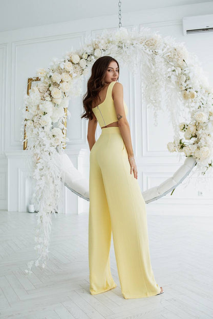 Woman in a yellow jumpsuit standing in front of a floral arch