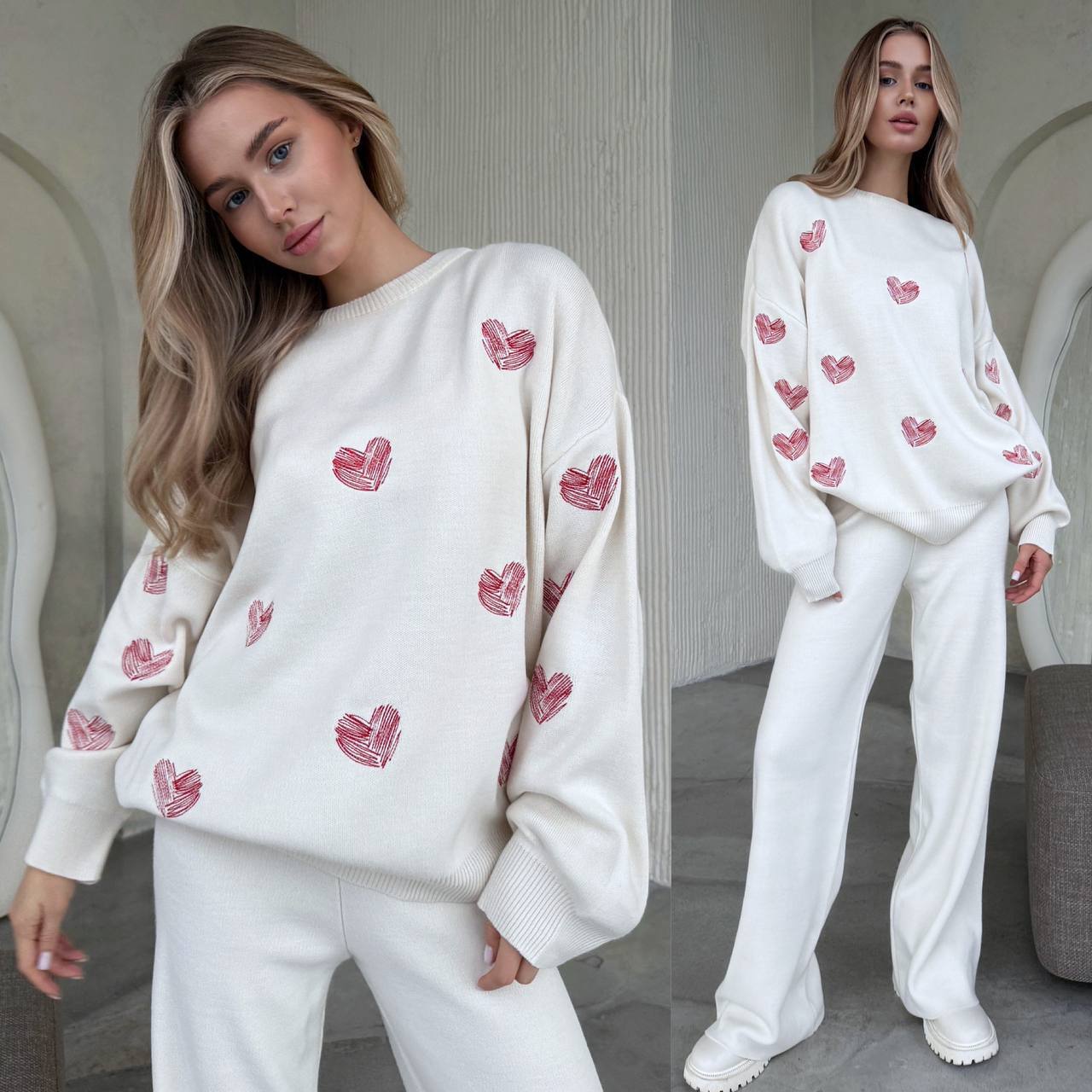 Woman wearing a white sweater with pink heart patterns and white pants indoors.