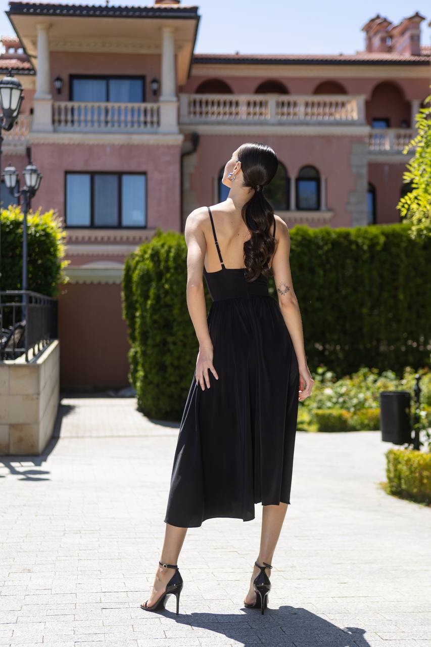 Woman in a black dress standing in front of a large building with a garden.