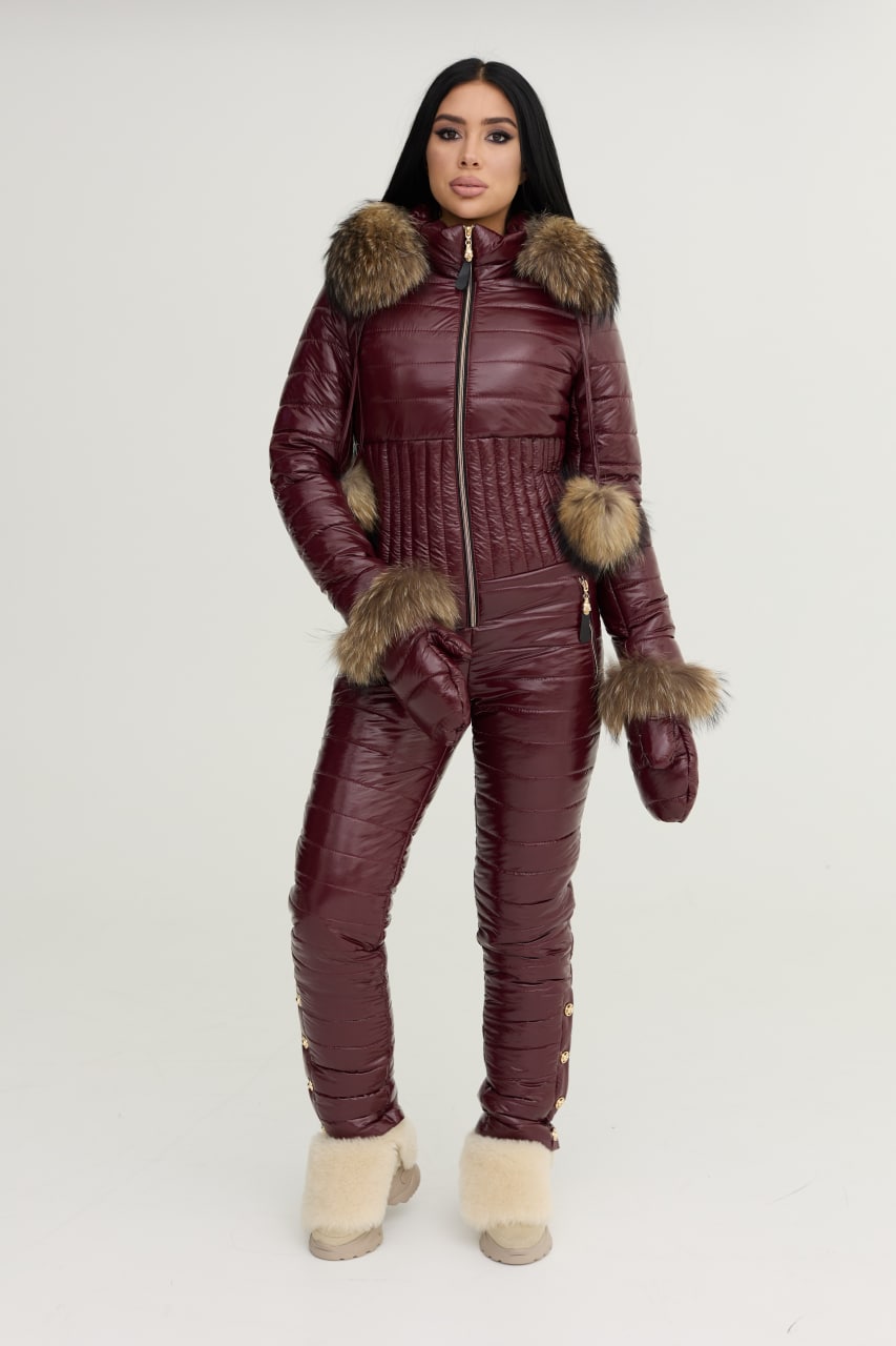 Person wearing a burgundy quilted jumpsuit with fur trim on a white background