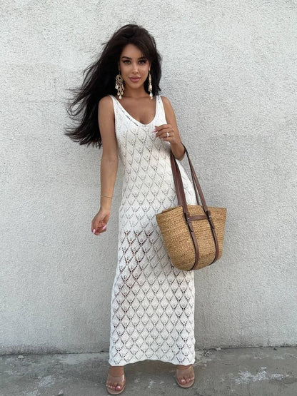 Woman in a white dress holding a straw bag against a light gray wall.