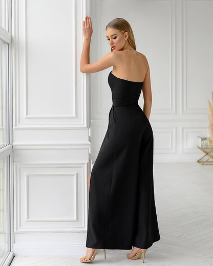 Woman wearing a black strapless jumpsuit in a white room.