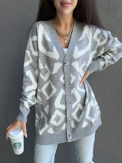 Person wearing a gray cardigan with white geometric pattern, holding a Starbucks cup against a plain background