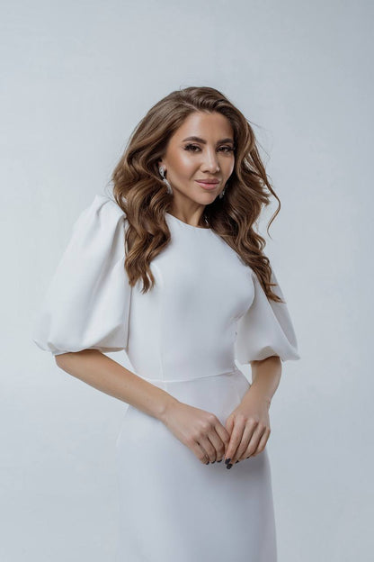 Woman wearing a white dress with puffed sleeves against a plain background