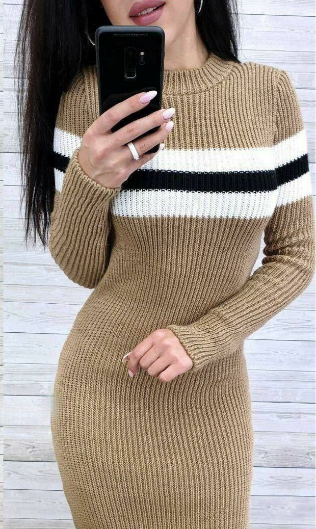 Person wearing a beige ribbed sweater dress with black and white stripes, holding a phone.