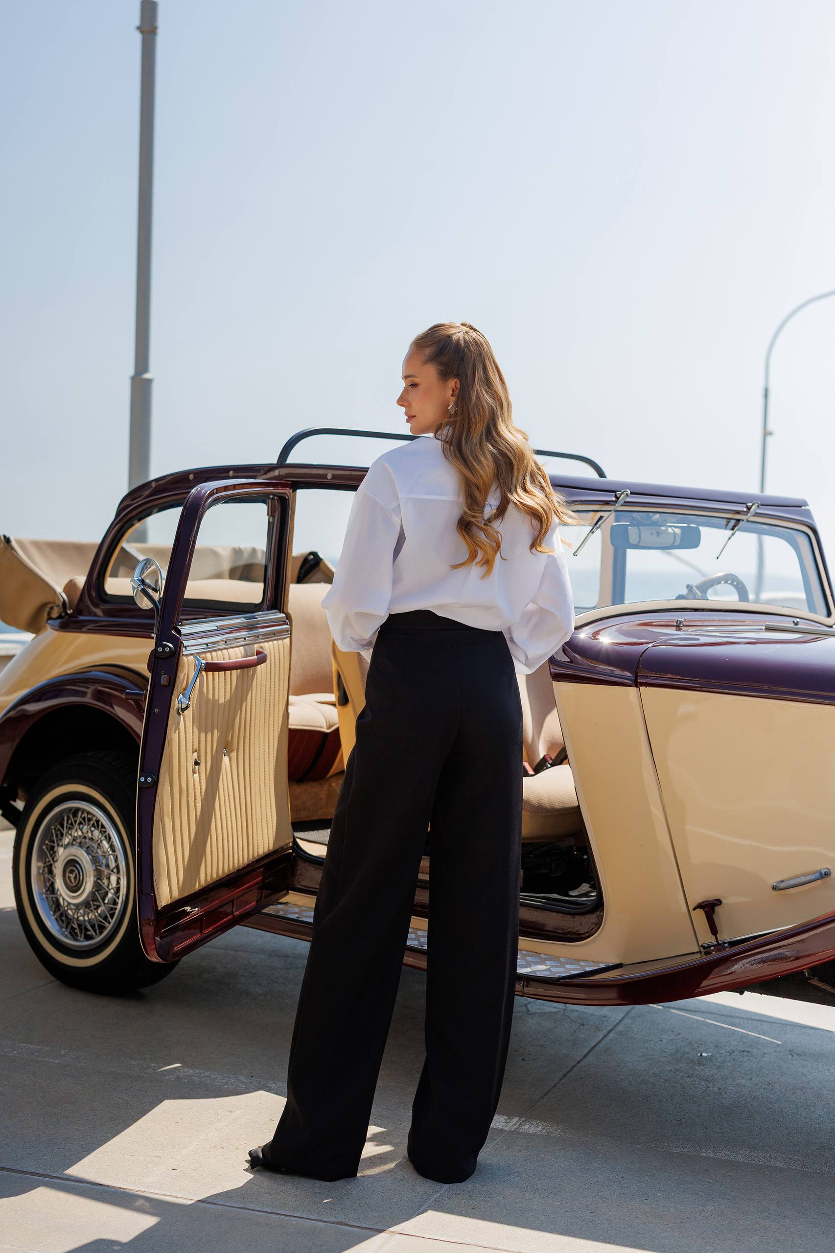 Woman standing next to a vintage car on a sunny day