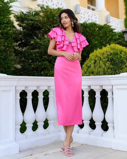 Woman in a pink dress with ruffled details standing on a balcony.