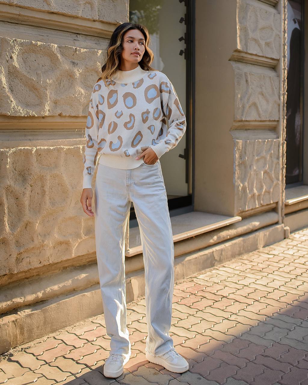 Person wearing a leopard print sweater and light blue jeans standing in front of a stone building.