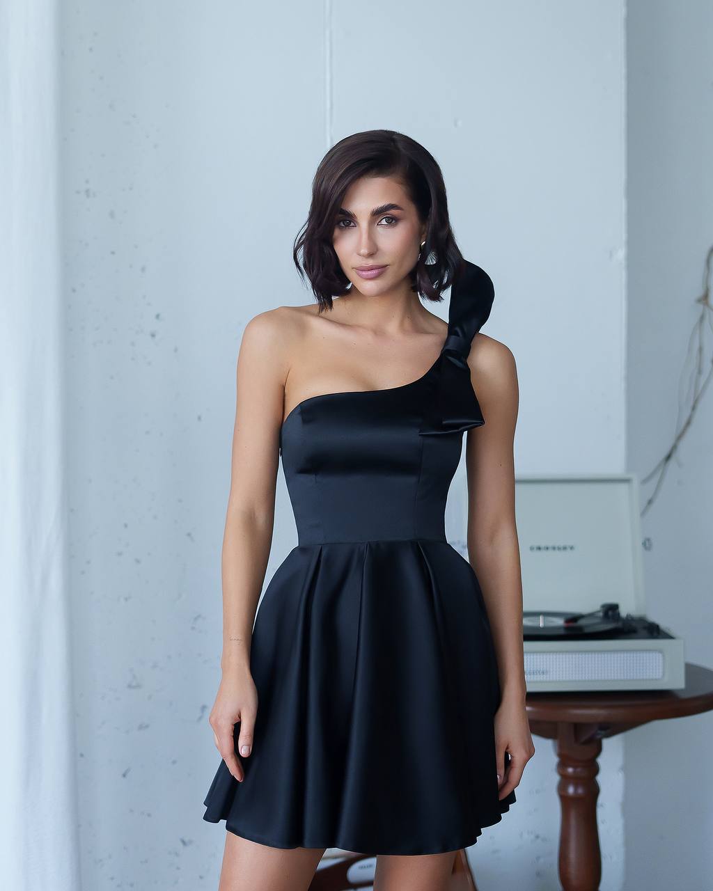 Woman wearing a black one-shoulder dress in a minimalistic setting.
