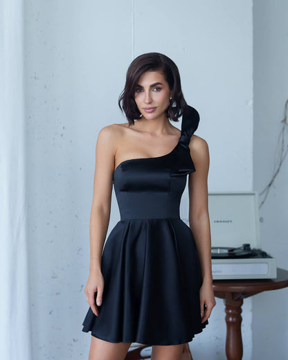 Woman wearing a black one-shoulder dress in a minimalistic setting.