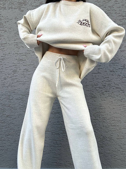 Person wearing a beige sweater and matching pants against a gray background