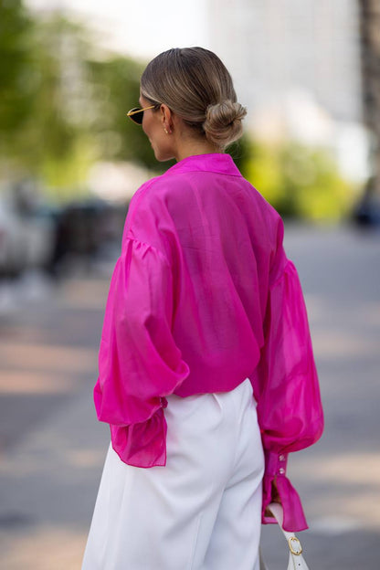 Person wearing a bright pink shirt and white pants on a blurred street background