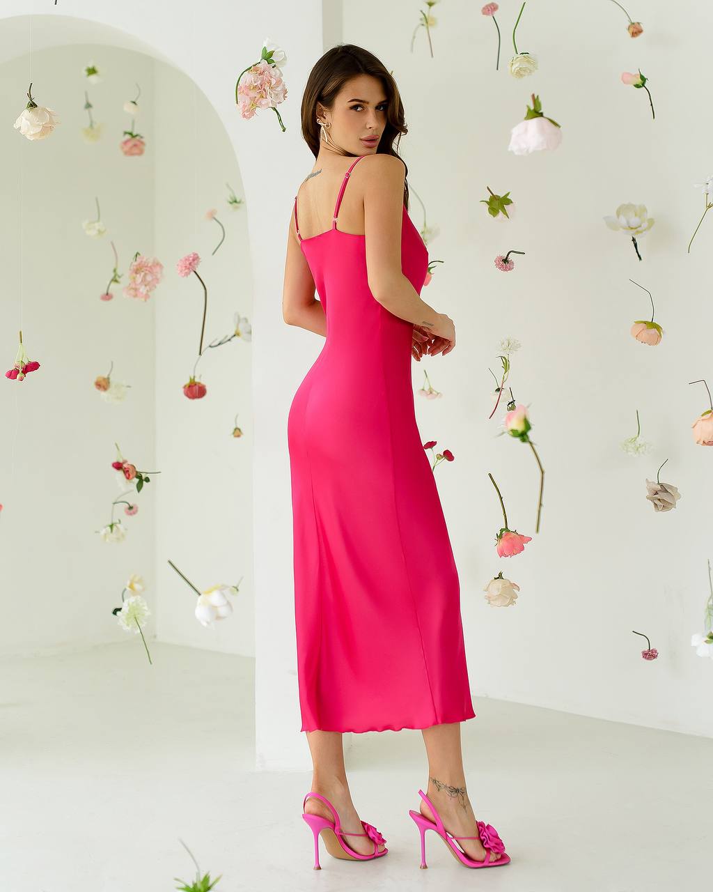 Woman in a bright pink dress standing against a white wall with decorative flowers.