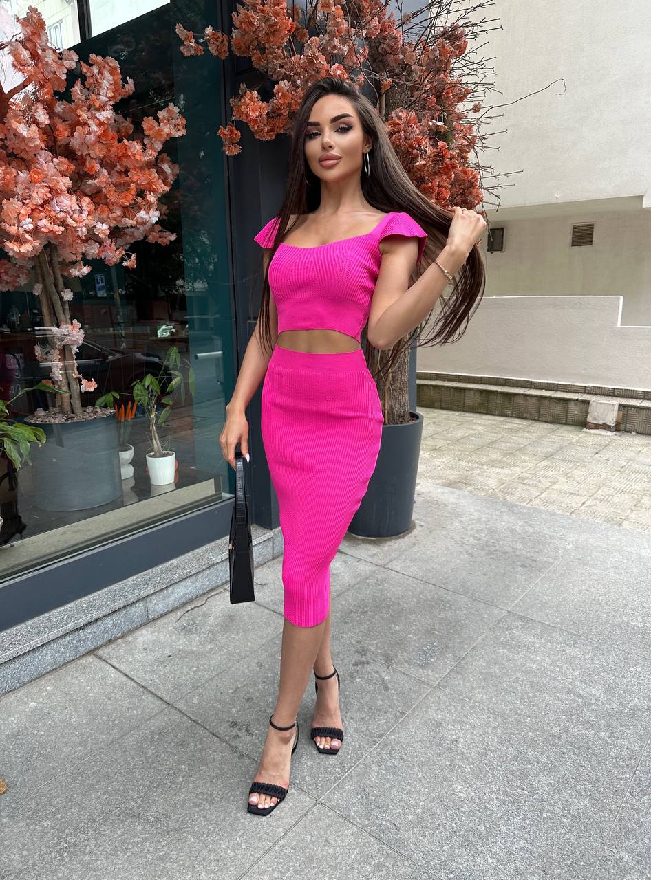 Woman in a bright pink outfit standing outdoors near a building entrance.