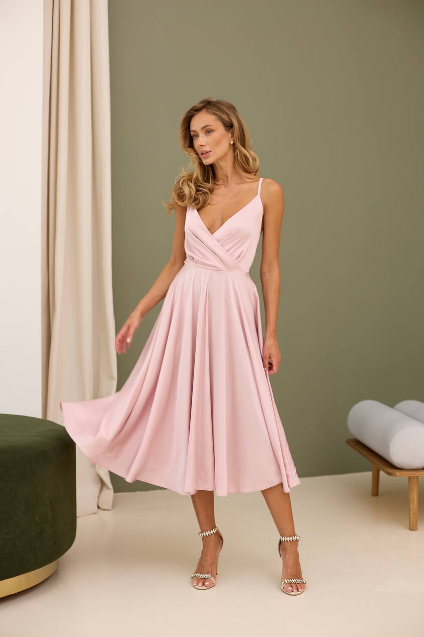 Woman wearing a pink dress in an indoor setting with a green wall and white curtain.