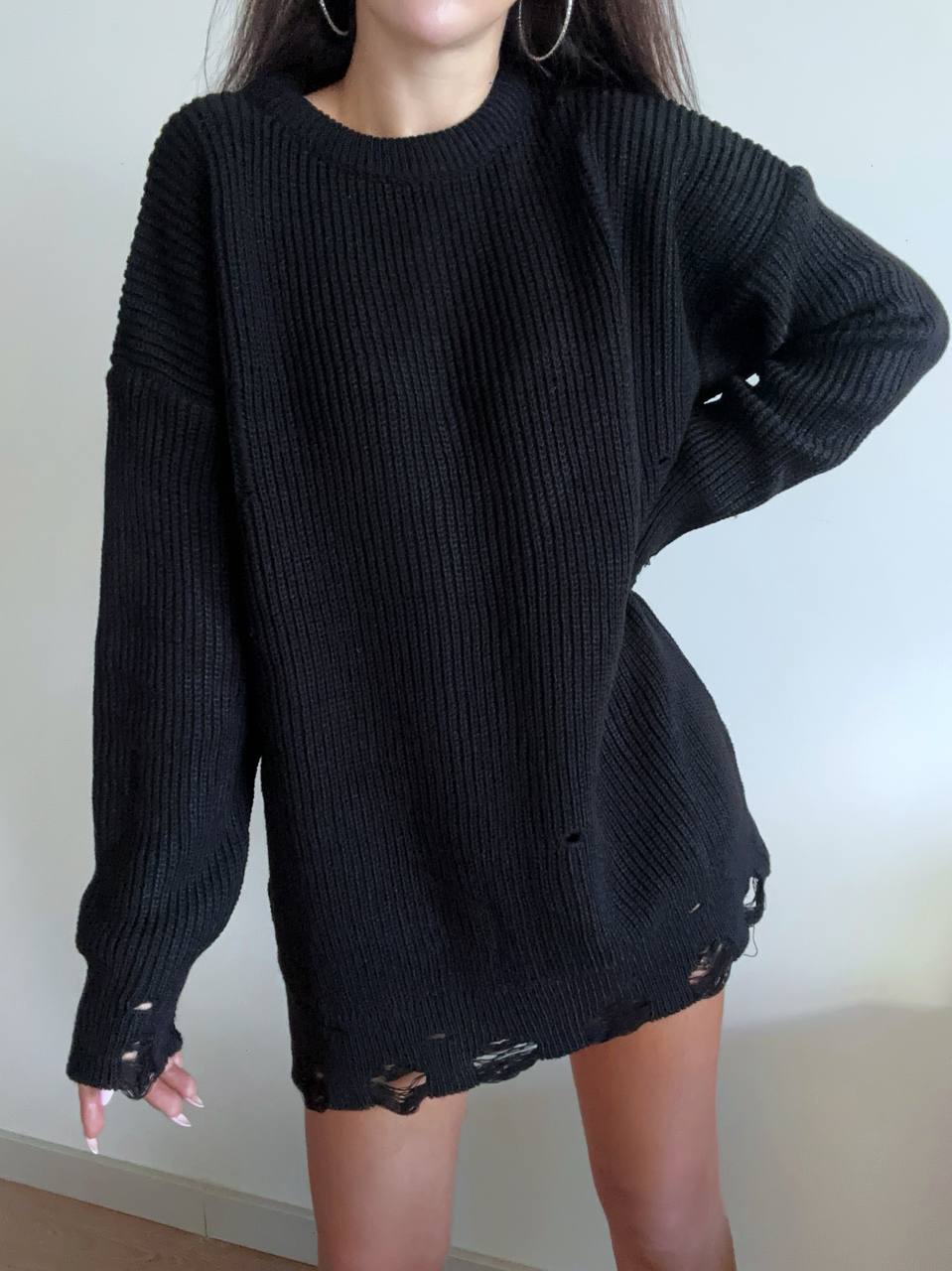 Person wearing a black oversized sweater with distressed details on a plain background