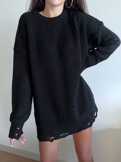 Person wearing a black oversized sweater with distressed details on a plain background