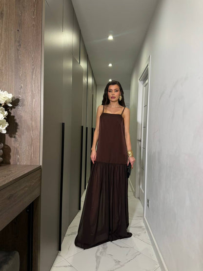 Woman in a long brown dress standing in a modern hallway.
