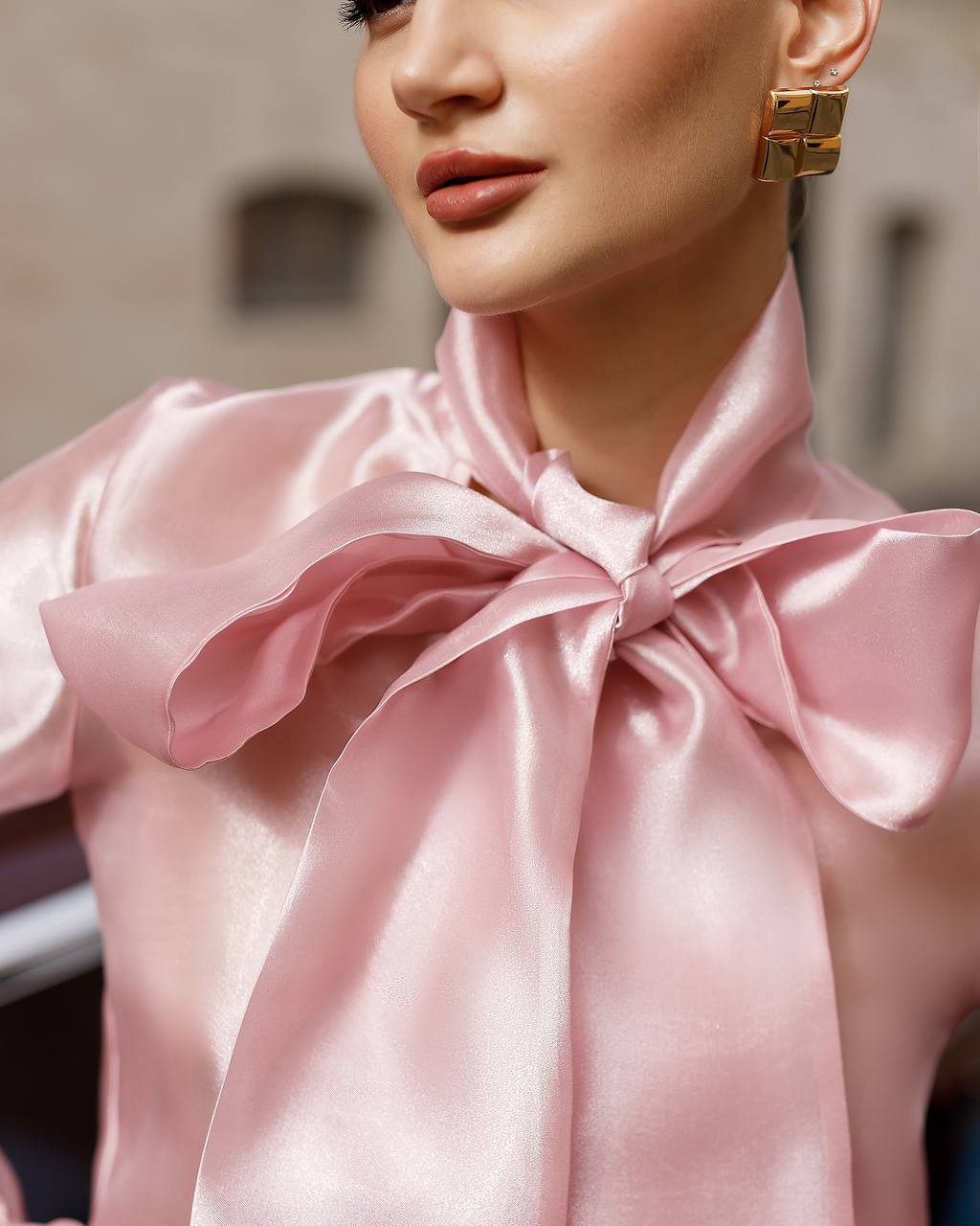 Close-up of a person wearing a pink satin blouse with a large bow detail.