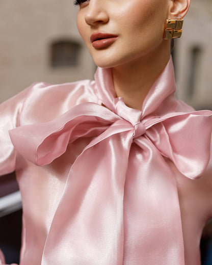 Close-up of a person wearing a pink satin blouse with a large bow detail.