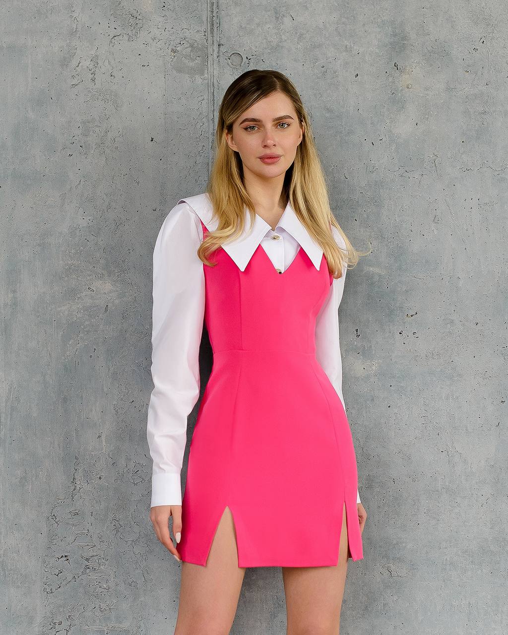 Woman wearing a pink dress over a white shirt against a gray concrete wall