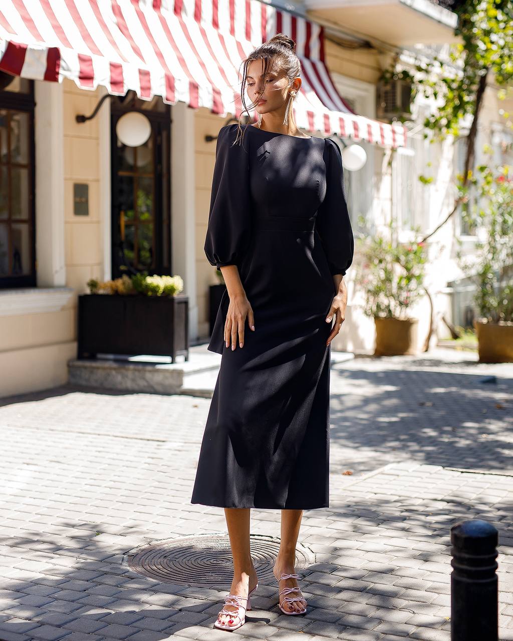 Woman in a black dress standing on a street with a striped awning in the background