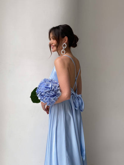 Woman in a light blue dress holding a bouquet of flowers against a plain background