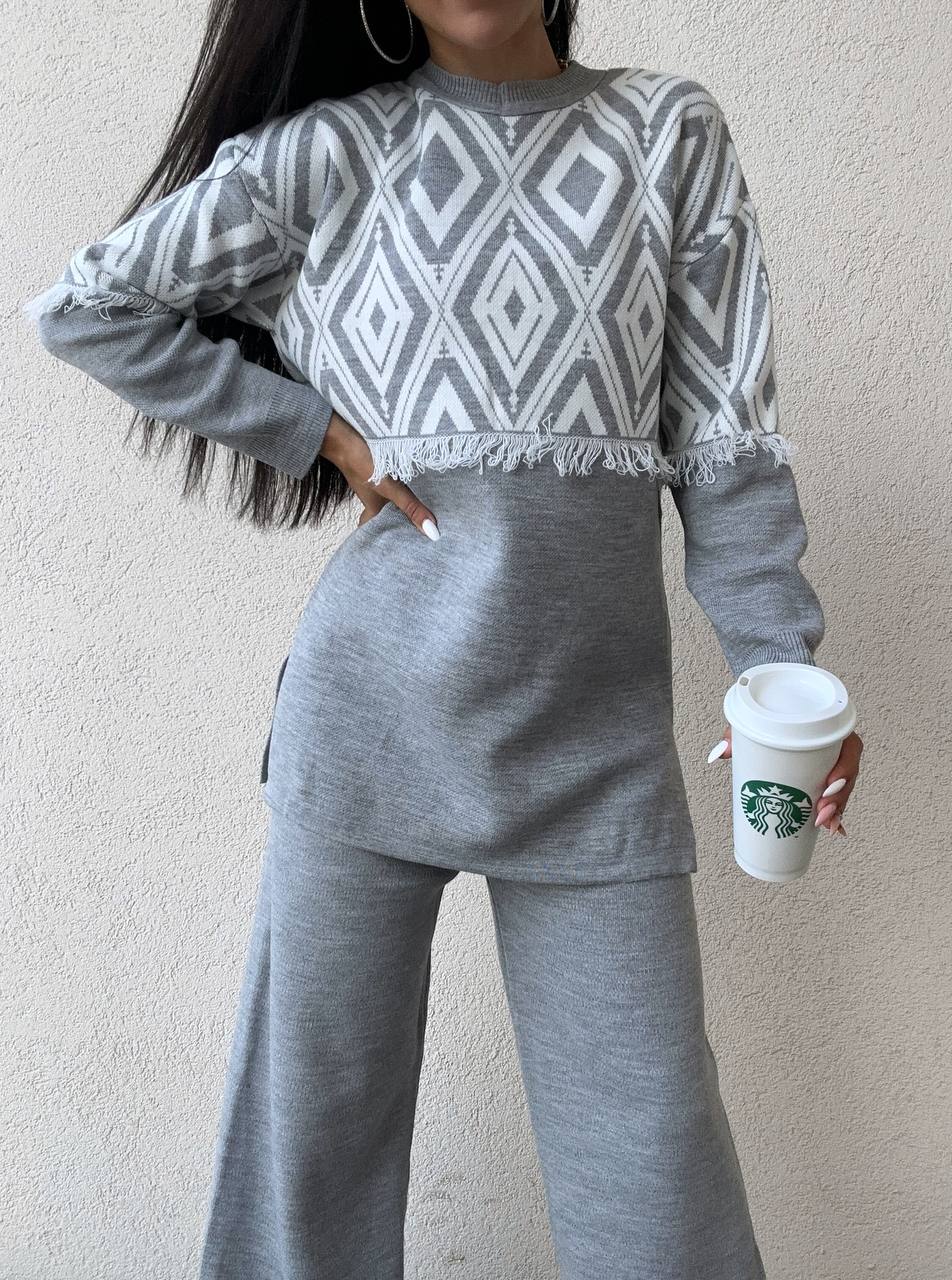 Person wearing a gray and white patterned sweater and matching pants, holding a Starbucks cup.