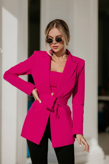Woman wearing a bright pink blazer and sunglasses outdoors.