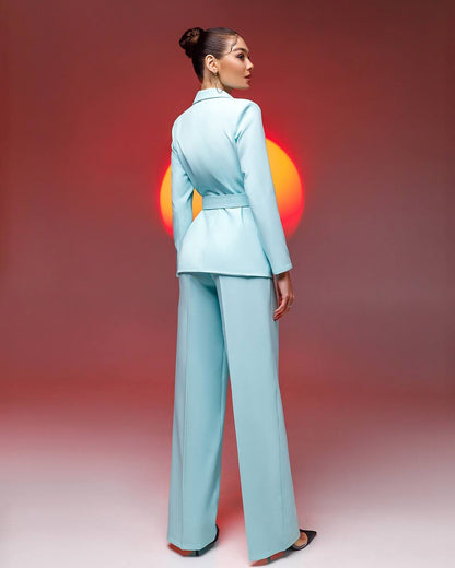 Woman in a light blue suit standing against a gradient background with a blurred circular object.