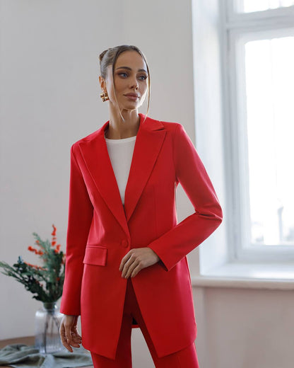 Woman wearing a red suit standing in a room with a window and plant.