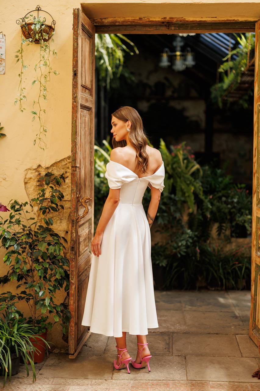 Woman in a white dress standing in an open doorway with plants around.