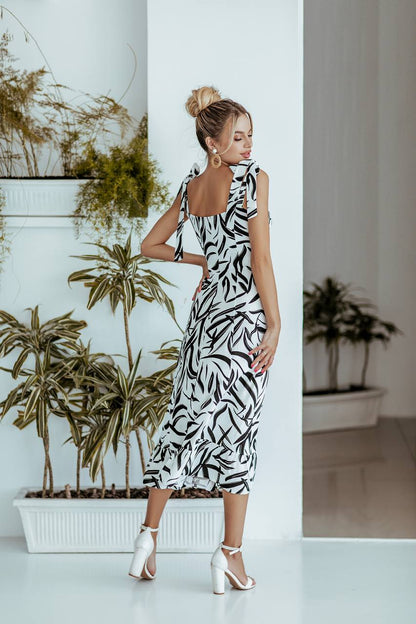 Woman in a black and white patterned dress standing in a room with plants.