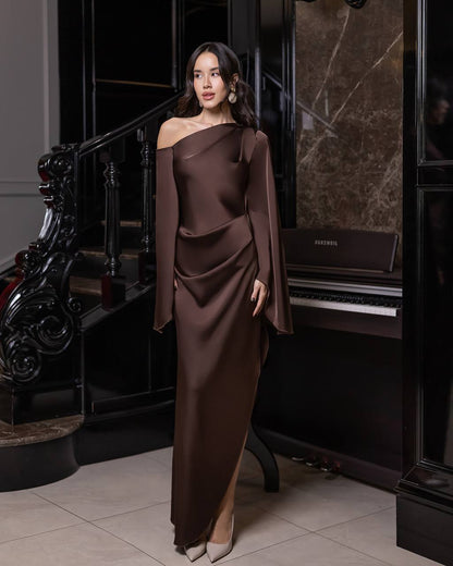 Woman in a brown off-shoulder dress standing in an elegant interior setting.