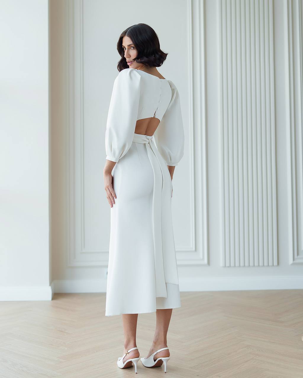 Woman wearing a white dress with cut-out design in a minimalistic room.