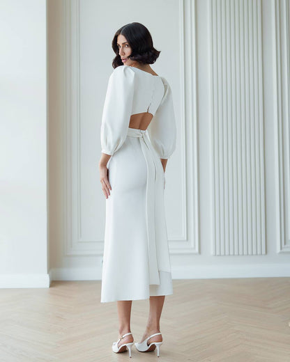 Woman wearing a white dress with cut-out design in a minimalistic room.