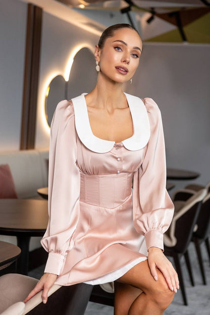 Woman wearing a light pink satin dress with a white collar in an indoor setting.