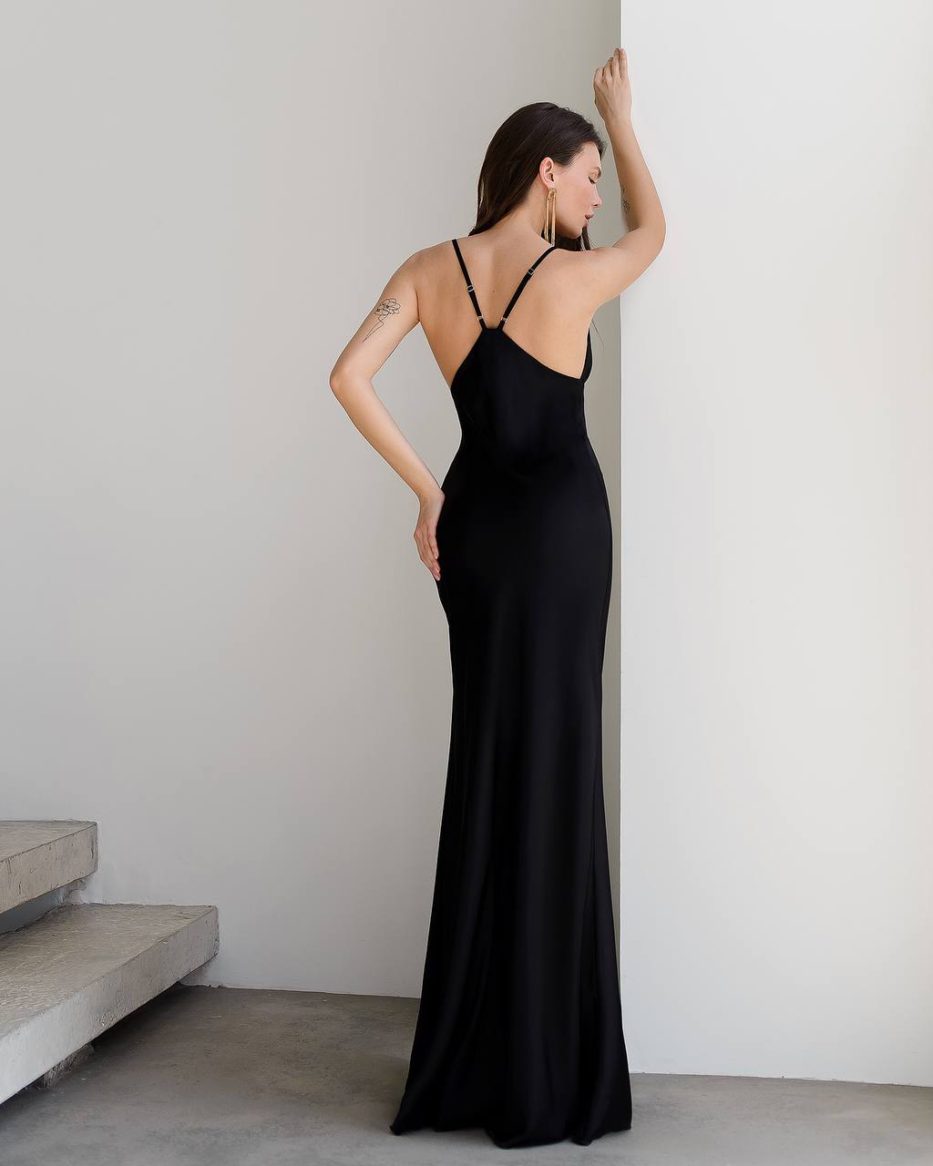 Woman wearing a black evening gown against a plain wall.