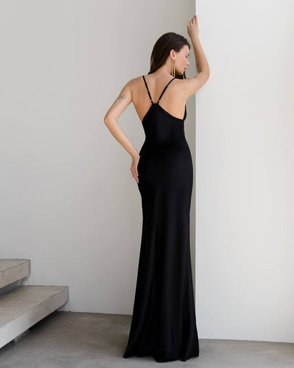 Woman wearing a black evening gown against a plain wall.