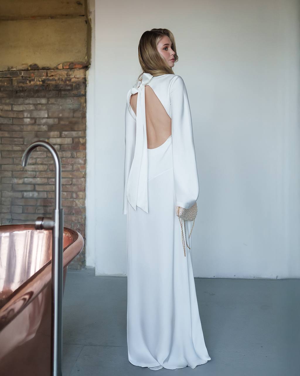 Woman wearing a white dress with a backless design in a minimalistic room.