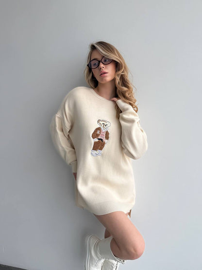 Woman wearing a cream-colored sweater with a graphic design against a plain background