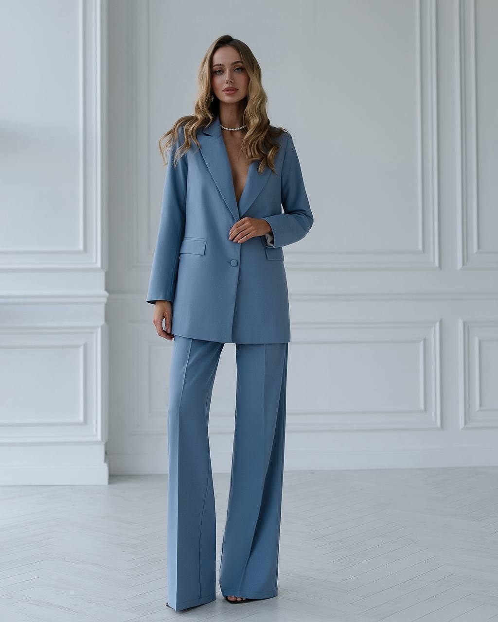 Woman wearing a blue suit standing against a white wall.