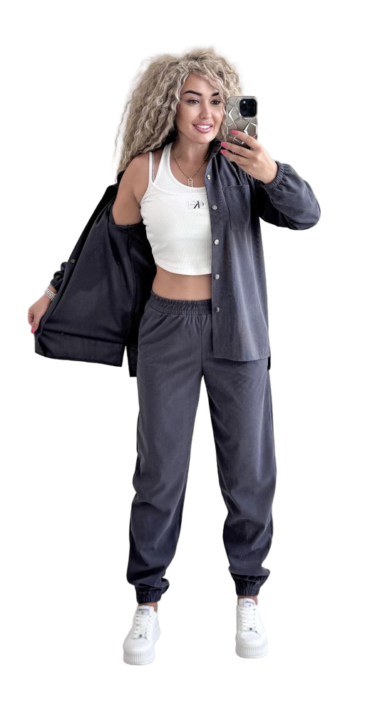 Woman in gray tracksuit with white sports bra taking a selfie on a white background
