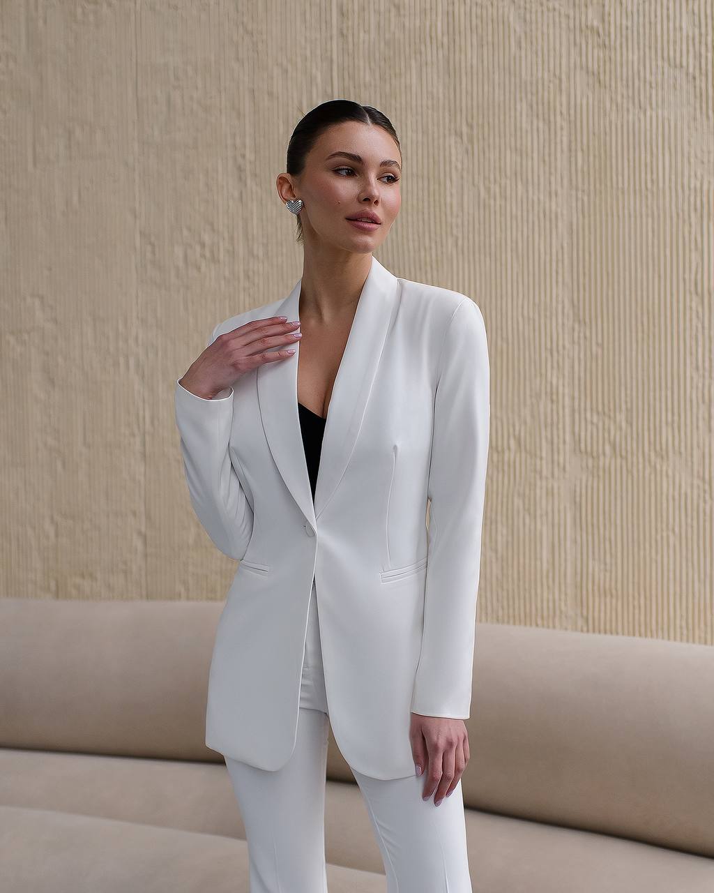 Woman wearing a white suit standing against a beige wall.
