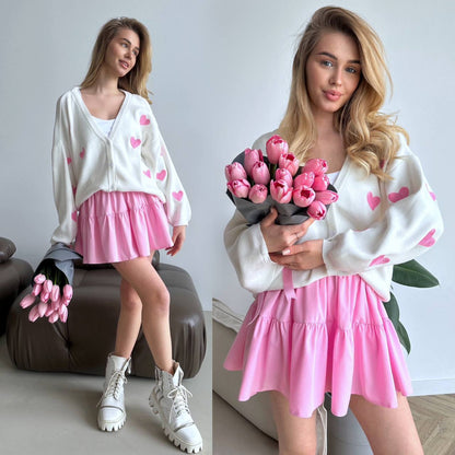 Woman in a white sweater with pink heart patterns and a pink skirt holding pink tulips.
