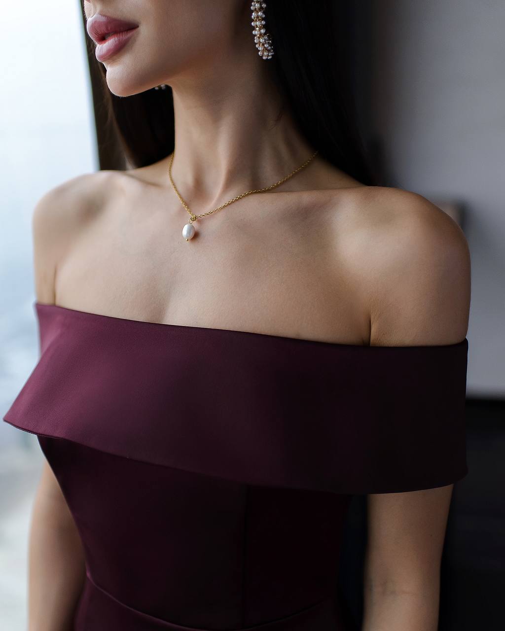 Woman wearing a burgundy off-shoulder dress with a gold necklace and earrings.