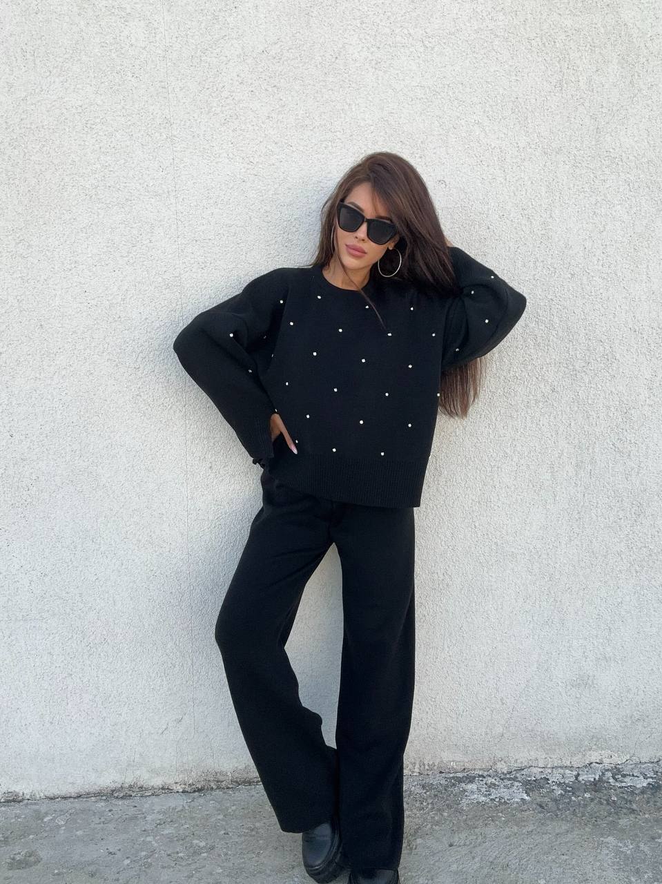 Person wearing a black outfit with white polka dots against a light gray wall.