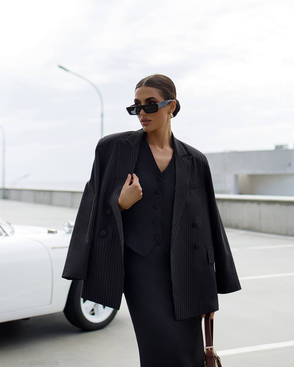 Person wearing a black outfit with sunglasses in front of a white vehicle