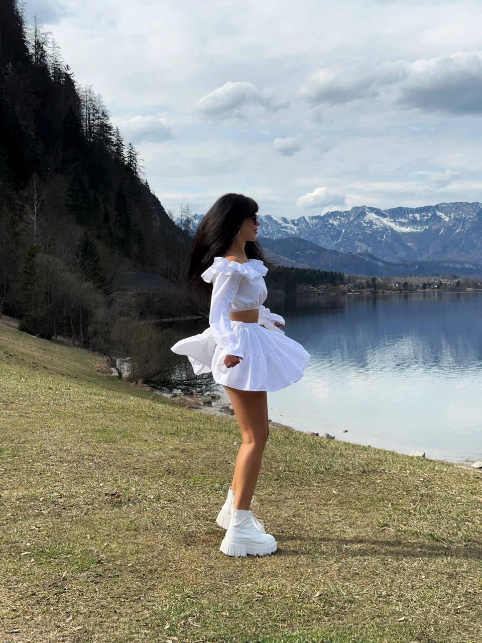 Woman in a white outfit standing by a lake with mountains in the background