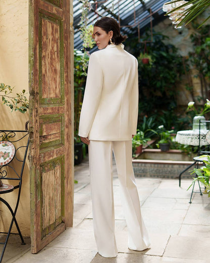 Woman in a white suit standing in a garden setting with a rustic door and plants.